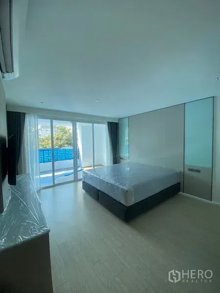 Apartment for rent in Watthana, Bangkok - Spacious bedroom with sliding glass doors opening to a balcony, ample daylight and minimalist furnishings.