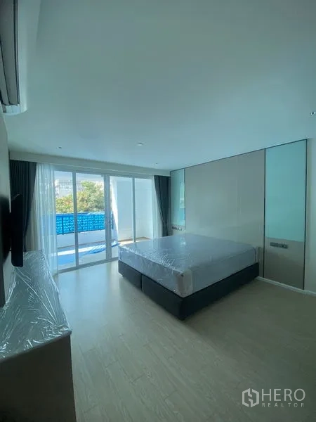 Apartment for rent in Watthana, Bangkok - Spacious bedroom with sliding glass doors opening to a balcony, ample daylight and minimalist furnishings.
