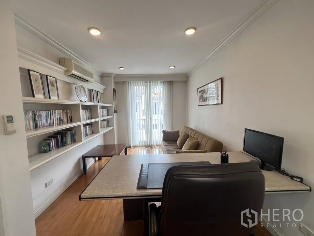 Townhouse for sale in Watthana, Bangkok - Home office with bookshelves, desk and sofa opening to a balcony.
