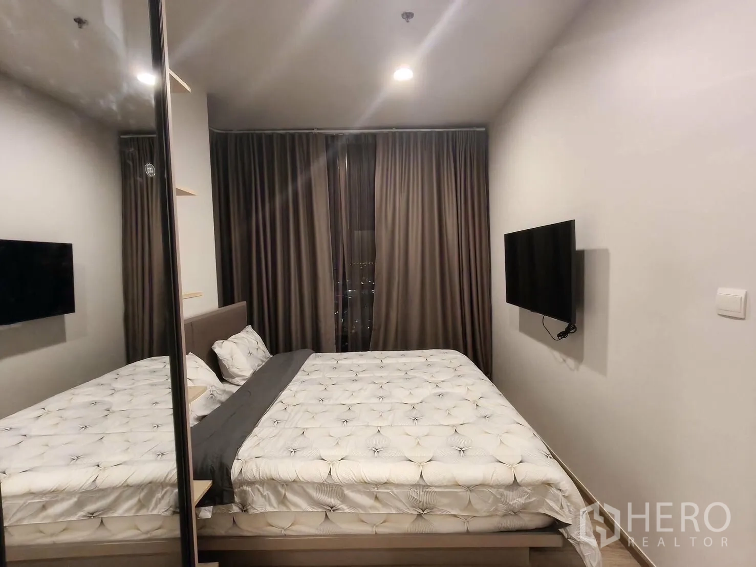 Condominium for rent in Khlong Toei, Bangkok - Master bedroom with upholstered bed, wall-mounted TV, mirrored wardrobe, and blackout curtains.
