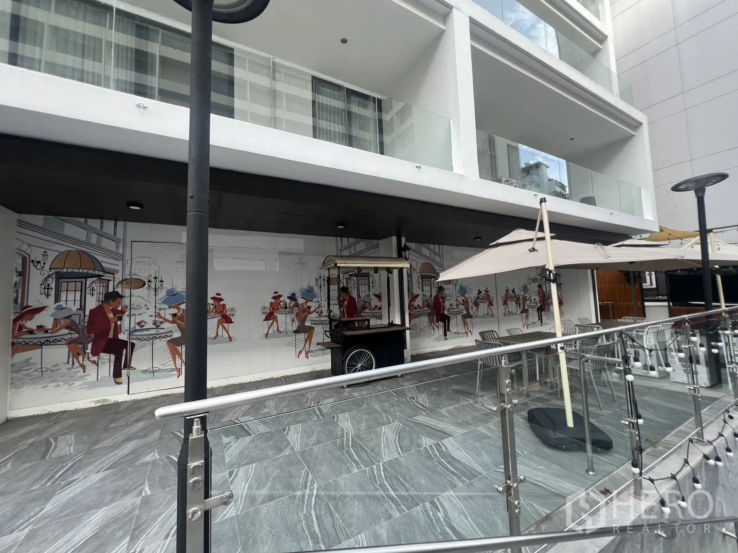 Retail Space for rent - Facade view of retail bay with glass rail, umbrellas and mural artwork along the plaza.