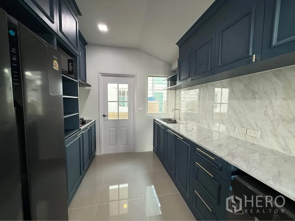 Semi-detached House for rent in Mueang Samut Prakan, Samut Prakan - Galley kitchen with dark blue cabinetry, marble-look countertops, and a window.