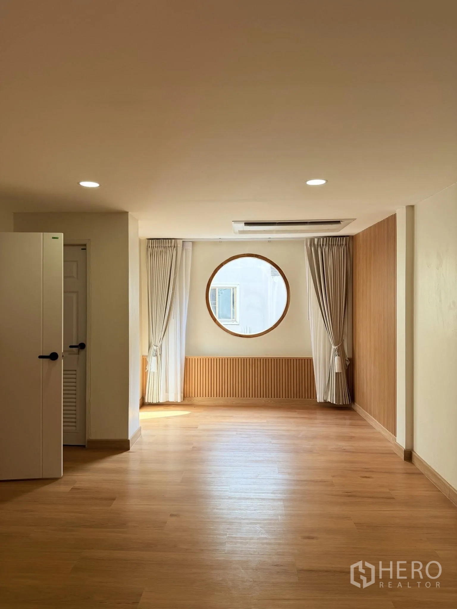 Townhouse for rent or sale in Yan Nawa, Bangkok - Bright living area with wood flooring, circular window, and curtains.