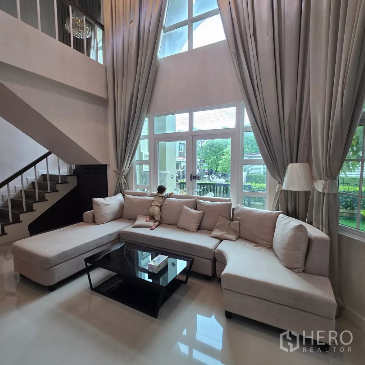 Detached House for rent in Mueang Pathum Thani, Pathum Thani - Bright living room with tall windows and long curtains opening to the terrace.