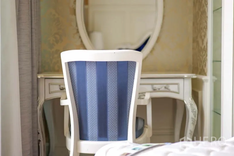 Condominium for rent in Khlong Toei, Bangkok - Dressing table with oval mirror and blue striped chair beside a curtained window.