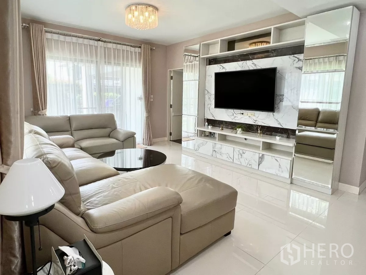 บ้าน ให้เช่าหรือขายในBang Phli, Samut Prakan - ห้องนั่งเล่นโมเดิร์น ผนังทีวีลายหินอ่อน โคมแชนเดอเลียร์ และโซฟาเข้ามุม.