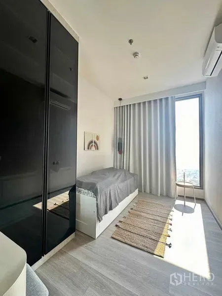 Condominium for rent in Bang Kho Laem, Bangkok - Bright secondary bedroom with single bed, glossy black wardrobe and floor-to-ceiling window behind light curtains.