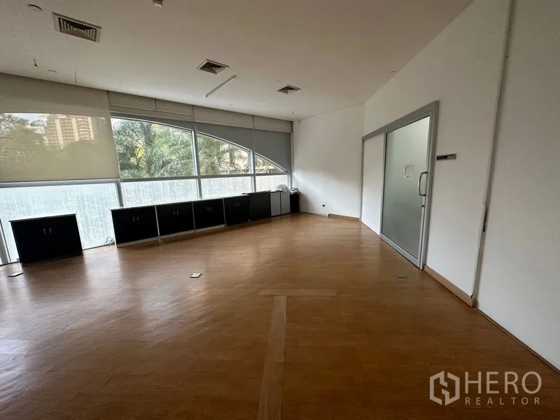 Office Space for rent in Pathum Wan, Bangkok - Spacious corner office with wood flooring, curved windows with blinds, and a glass meeting room door.