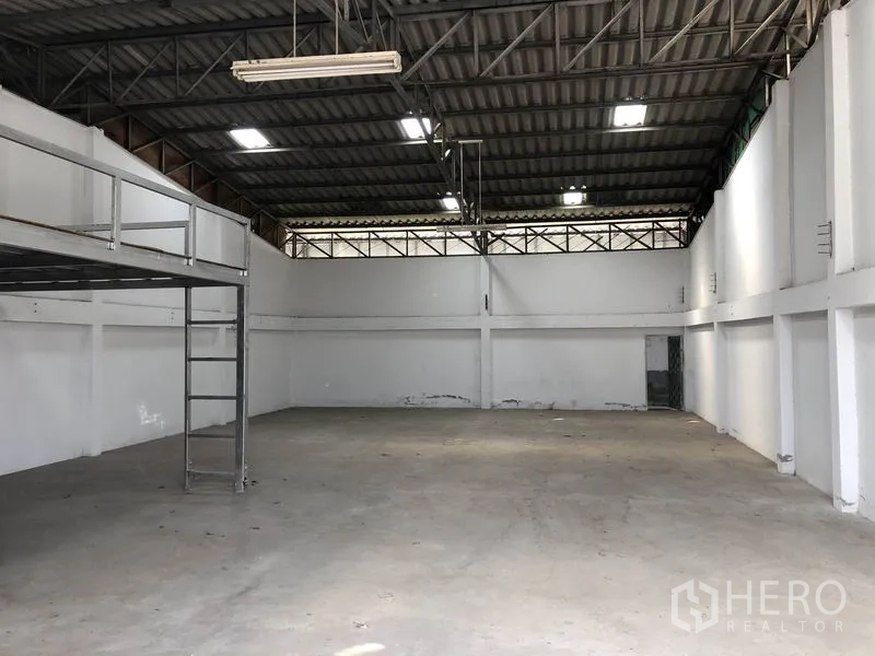 Warehouse for rent or sale in Khlong Luang, Pathum Thani - Spacious warehouse interior with high steel-truss roof, bright ceiling lights, concrete floor, and a mezzanine platform with ladder.