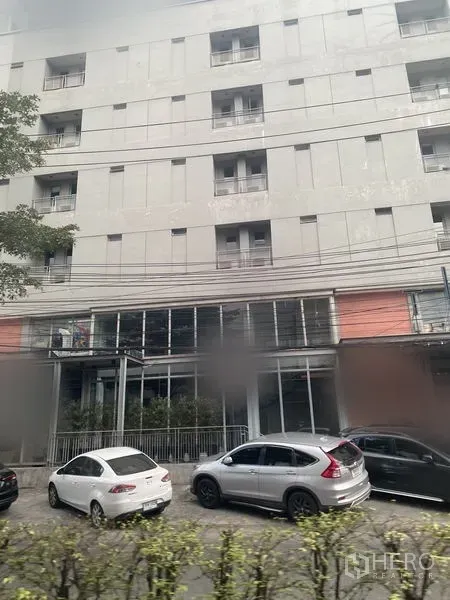 Retail Space for rent in Watthana, Bangkok - Modern mid-rise building with ground-floor glass retail frontage and cars parked along the street.