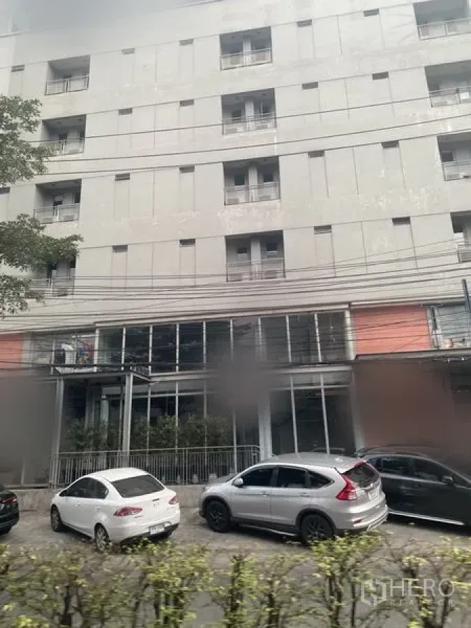 Retail Space for rent in Watthana, Bangkok - Modern mid-rise building with ground-floor glass retail frontage and cars parked along the street.