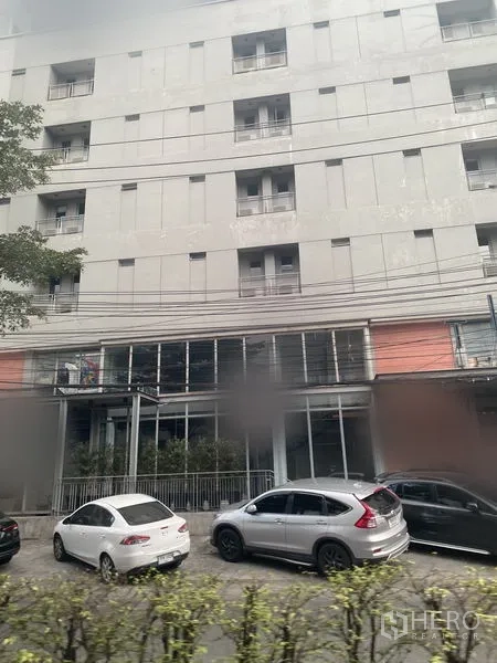 Retail Space for rent in Watthana, Bangkok - Modern mid-rise building with ground-floor glass retail frontage and cars parked along the street.