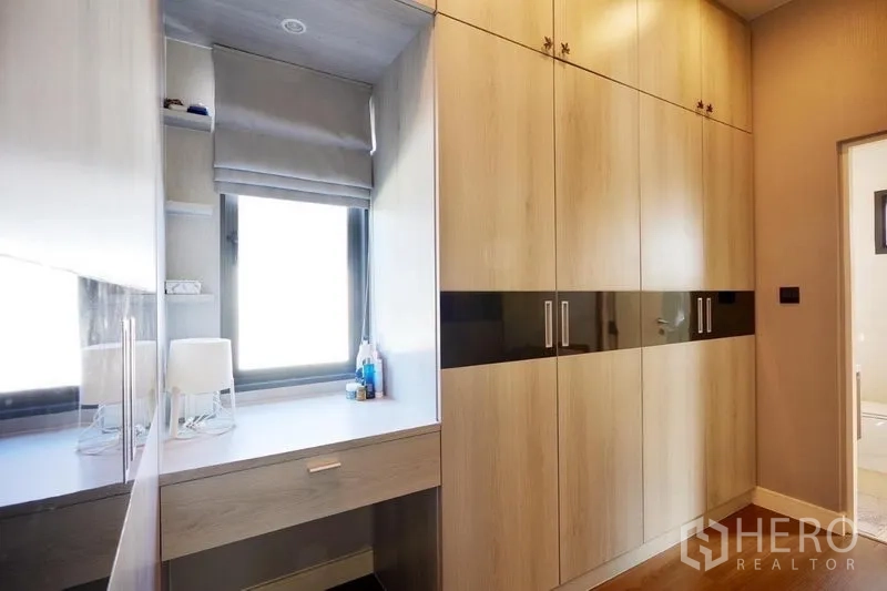 Detached House for rent or sale in Bang Kapi, Bangkok - Walk-in closet corridor with full-height cabinetry and a vanity by the window.