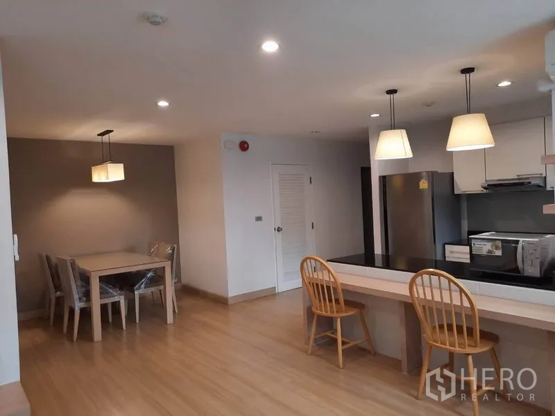 Condominium for rent in Watthana, Bangkok - Dining area with four-seat table beside the open kitchen, pendant lighting, large refrigerator and counter space.