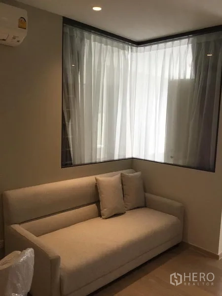 Condominium for rent in Watthana, Bangkok - Corner sofa beneath sheer curtains beside a glass partition in the modern condo living area.