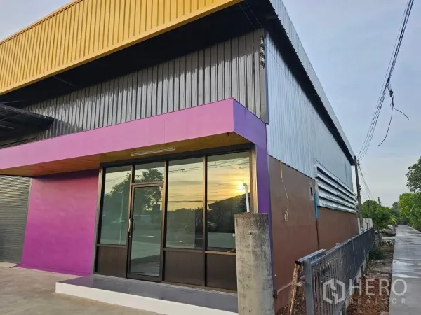 货栈 出租在Lam Luk Ka, Pathum Thani - 建筑转角展示带紫色饰带的玻璃办公室入口与黄色屋檐。