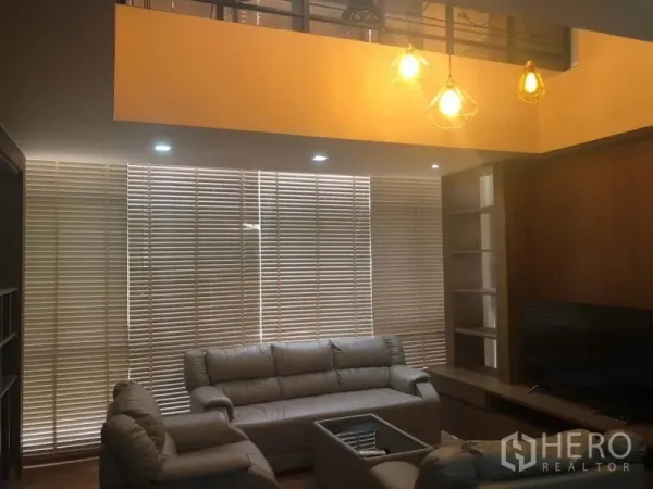 Condominium for sale in Bang Na, Bangkok - Cozy living room with high ceiling, pendant lights, leather sofas, media cabinet and full-width Venetian blinds.