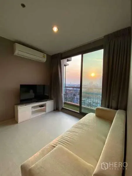 Condominium for rent or sale in Khlong Toei, Bangkok - Cozy lounge with cream sofa, TV console and sliding glass doors opening to a balcony with skyline views.