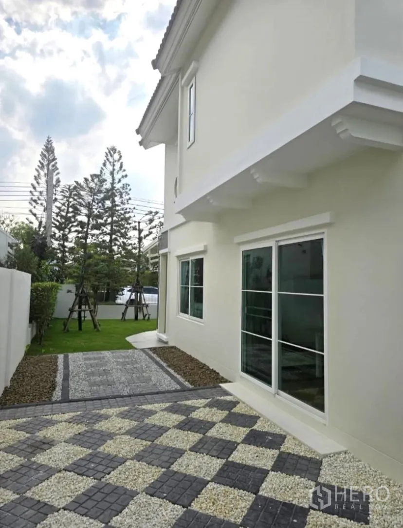 独立式住宅 for rent in Bang Phli, Samut Prakan - 房屋侧院，铺有图案石道与白色外墙相邻。