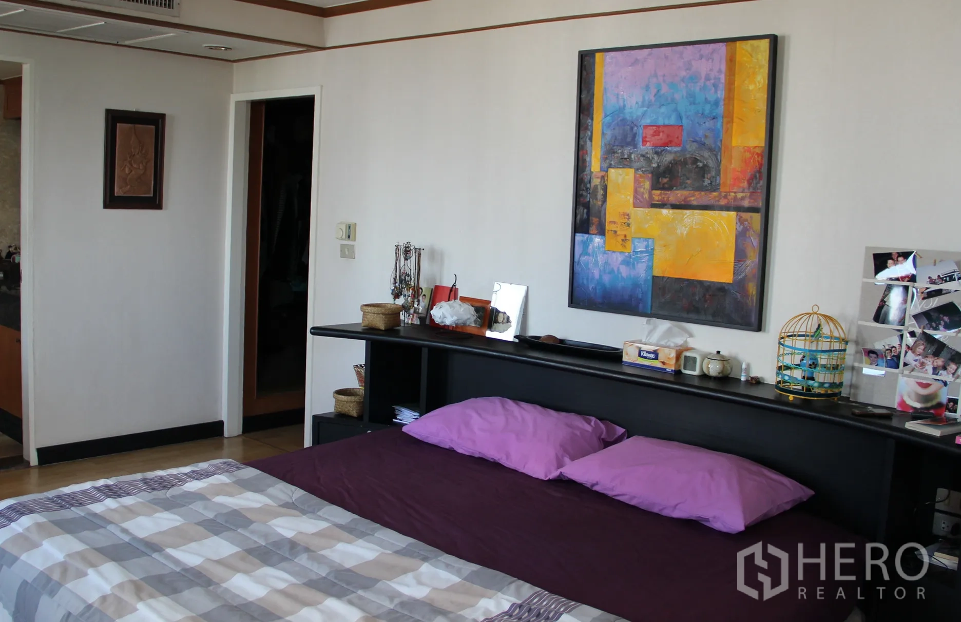 Condominium for rent in Khlong Toei, Bangkok - Master bedroom with a large bed, built-in headboard shelf, and colorful artwork.