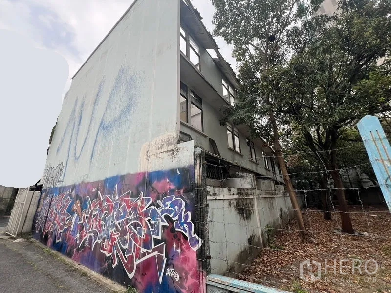 Land for rent in Watthana, Bangkok - Side wall with colorful graffiti next to a fenced lane and mature trees.