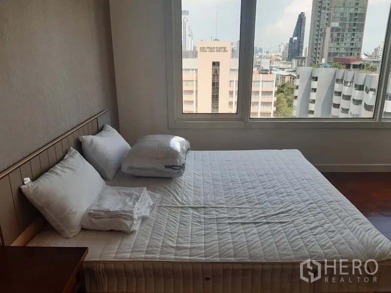 Condominium for rent in Khlong Toei, Bangkok - Master bedroom with large windows, city skyline outlook, and a neatly made bed.