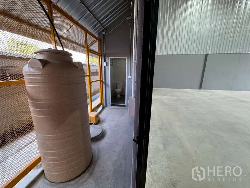 Warehouse for rent in Bang Phli, Samut Prakan - Service corridor with a water tank and mesh fencing beside the warehouse interior