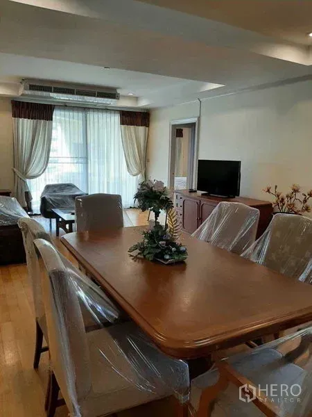 Apartment for rent in Watthana, Bangkok - Open-plan living and dining with floor-to-ceiling curtains, TV console, and access to a bright balcony.