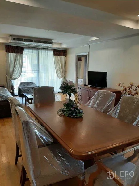 Apartment for rent in Watthana, Bangkok - Open-plan living and dining with floor-to-ceiling curtains, TV console, and access to a bright balcony.