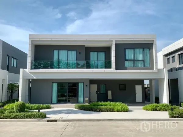 บ้าน ขาย - ภาพภายนอกบ้านสองชั้นสมัยใหม่ ระเบียง หน้ากว้างสีเทาขาว ที่จอดรถในร่ม และสวนหย่อม
