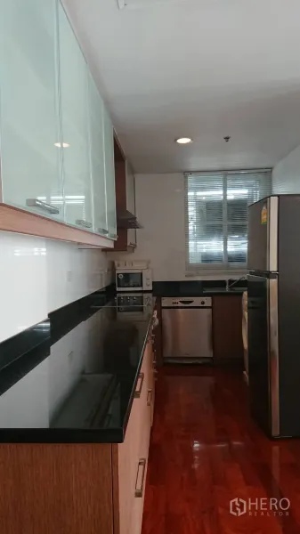 公寓 出租在Pathum Wan, Bangkok - 廊式厨房，黑色花岗岩台面、玻璃门吊柜，不锈钢冰箱、洗碗机与微波炉，旁有窗户。