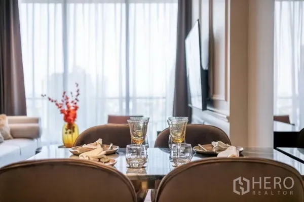 Condominium for rent in Khlong Toei, Bangkok - Elegant dining table set for four next to full‑height windows and a TV wall.
