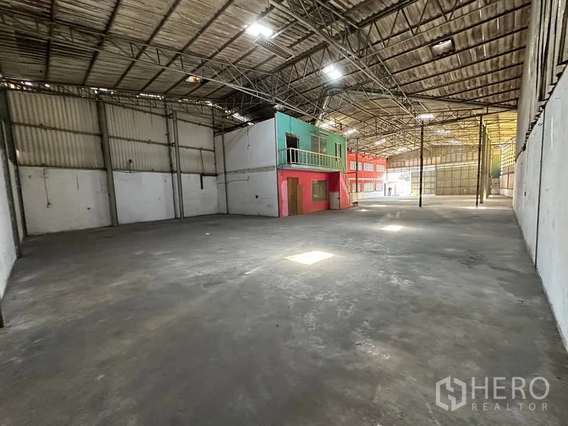 货栈 出租在Suan Luang, Bangkok - 纵深仓库空间，混凝土地面，侧设办公室，尽头为宽幅卷帘门。