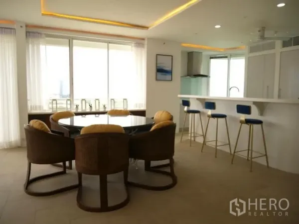 Condominium for rent in Khlong Toei, Bangkok - Round dining table and breakfast bar with blue stools beside large windows.