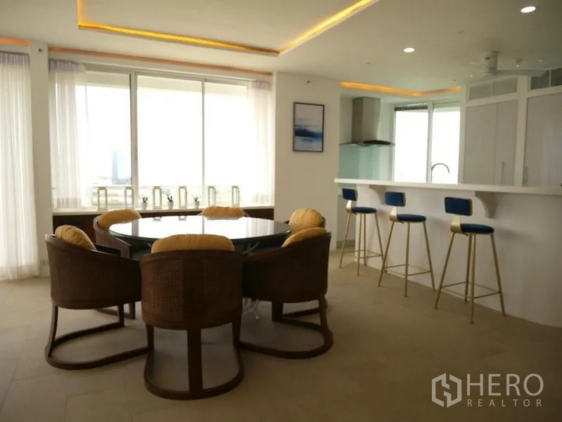 Condominium for rent in Khlong Toei, Bangkok - Round dining table and breakfast bar with blue stools beside large windows.
