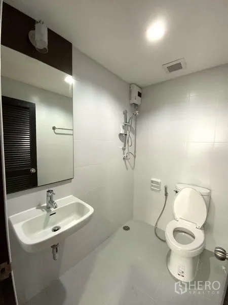 公寓 出租在Watthana, Bangkok - 现代卫浴，壁挂式洗手盆、马桶与带热水器的淋浴区。