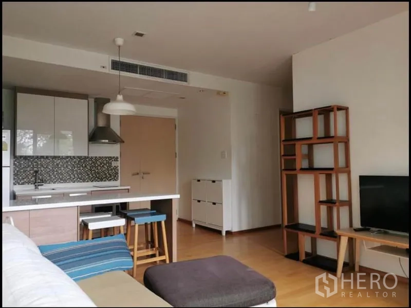 Condominium for rent in Khlong Toei, Bangkok - Living area with sofa, TV shelf, breakfast bar, and open kitchen.