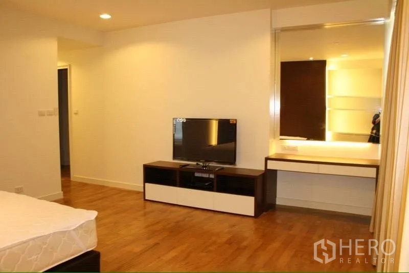 Condominium for rent in Watthana, Bangkok - Bedroom corner with flat-screen TV on console and a vanity desk, light wood flooring and soft lighting.