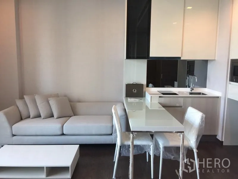 公寓 出租在Watthana, Bangkok - 开放式起居区，浅灰色沙发、餐桌椅与带电磁炉和水槽的小厨房。