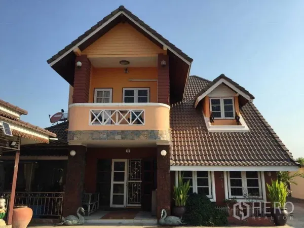 Detached House for rent or sale in Bang Bua Thong, Nonthaburi - Front exterior of a two-storey detached house with balcony, gabled tile roof and potted plants.