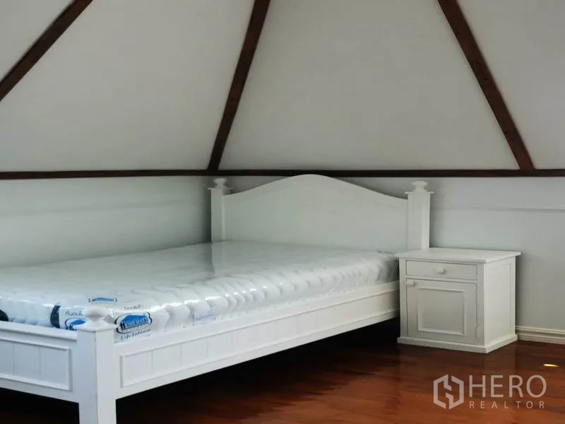 Detached House for rent in Mueang Samut Prakan, Samut Prakan - Bedroom under a pitched ceiling with a white bed frame and bedside table.