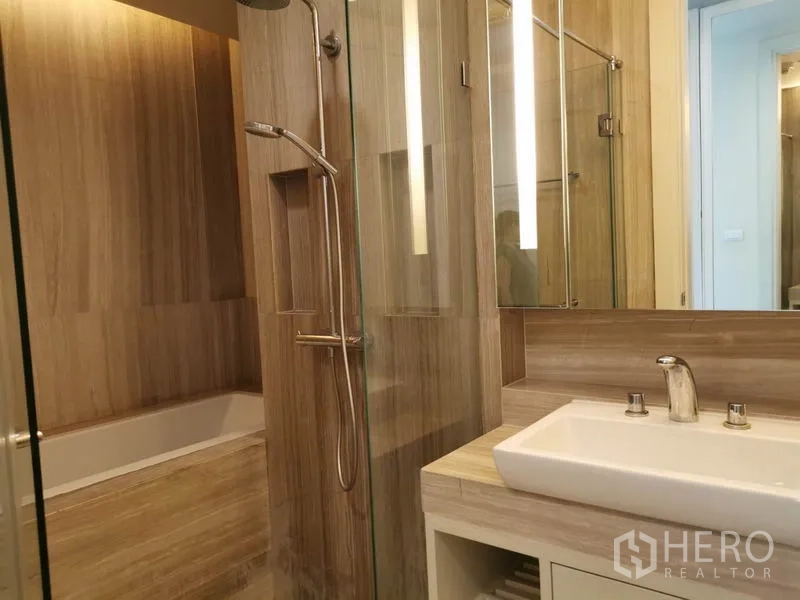 Condominium for rent in Pathum Wan, Bangkok - Contemporary bathroom with glass shower and separate bathtub in wood tones.