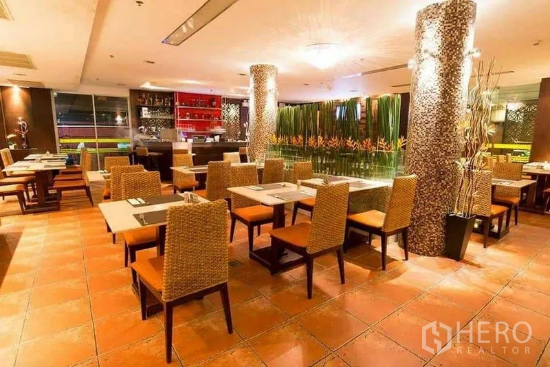 零售空间 出租在Khlong Toei, Bangkok - 餐厅内部朝向吧台，绿植隔断与橙色座椅。