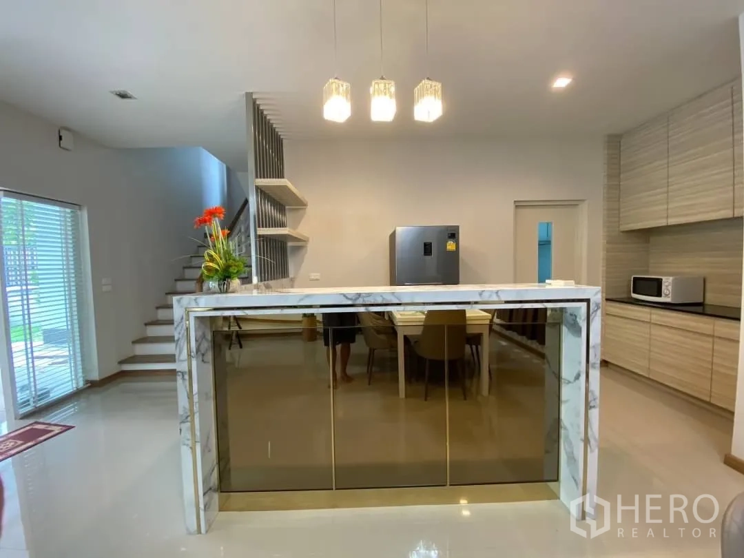 Detached House for rent or sale in Prawet, Bangkok - Open kitchen with a marble island, pendant lights and stairs leading to the upper floor.