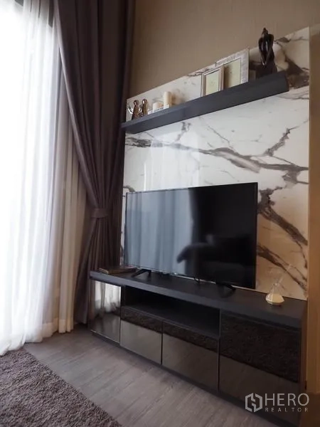 Condominium for rent in Khlong San, Bangkok - Living room TV console on a marble feature wall with shelf and long drapes.