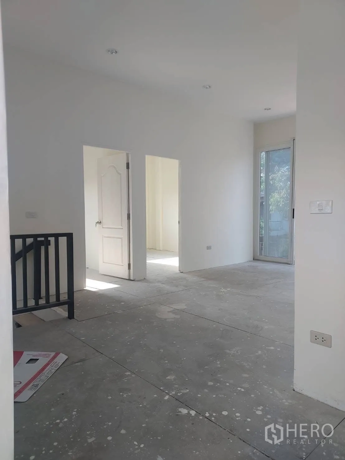 บ้านเดี่ยว for rent in Watthana, Bangkok - โถงชั้นบนสว่างผนังสีขาว พื้นคอนกรีต และประตูบานเลื่อนมองเห็นต้นไม้ด้านนอก.