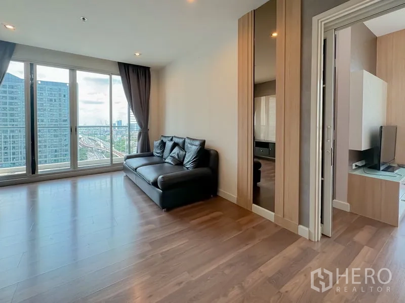 Condominium for sale - Living room seating with black leather sofa beside large windows and balcony.