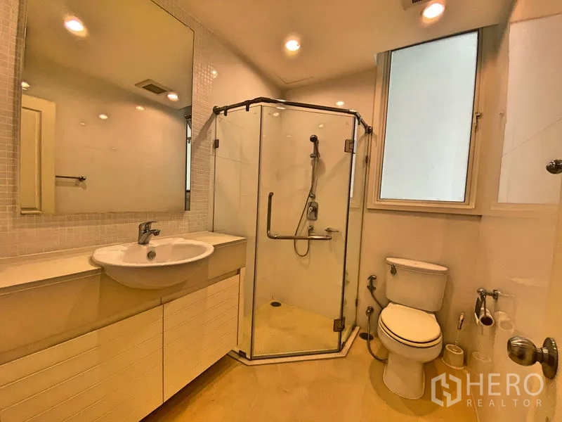 Condominium for rent in Khlong Toei, Bangkok - Second bathroom with corner glass shower, vanity, toilet and window.