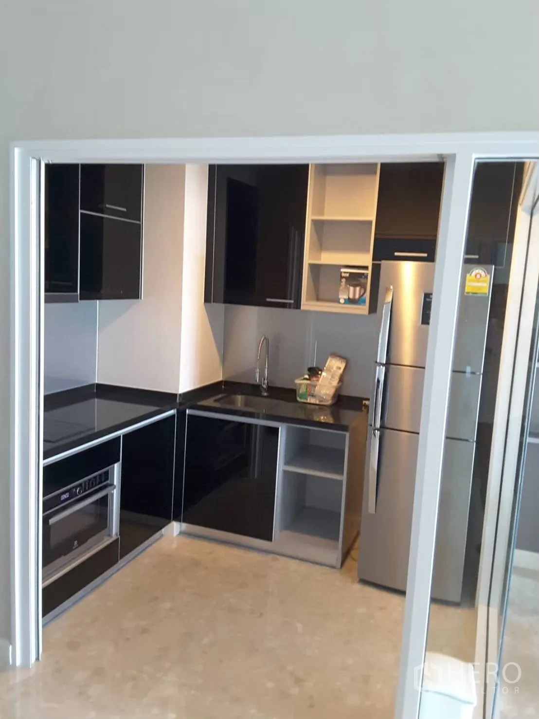 Condominium for rent in Khlong Toei, Bangkok - Compact L-shaped kitchen with black cabinetry, built-in oven, and refrigerator.