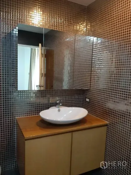 Condominium for rent in Phaya Thai, Bangkok - Bathroom vanity with vessel sink on a wooden cabinet and brown mosaic tile walls.